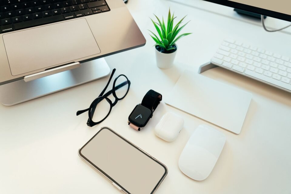 Smartphone bersama smartwatch, earbud, mouse, laptop, dan aksesori teknologi lain di atas meja putih