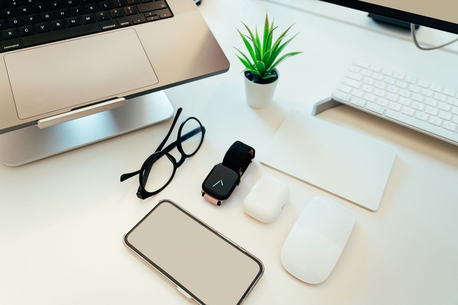 Smartphone bersama smartwatch, earbud, mouse, laptop, dan aksesori teknologi lain di atas meja putih