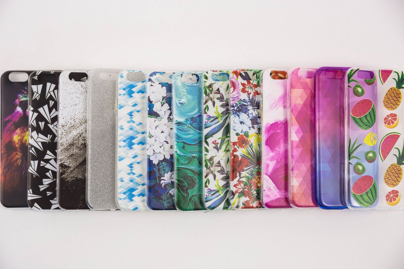 Beragam casing iPhone berwarna-warni dengan pola berbeda tersusun berjajar di atas permukaan putih