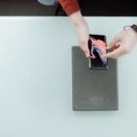 Seseorang memeriksa smartphone di atas meja dengan kedua tangan