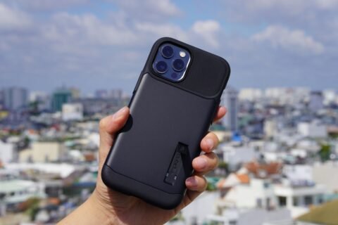 Tangan memegang iPhone bercasing hitam di depan pemandangan kota pada siang hari