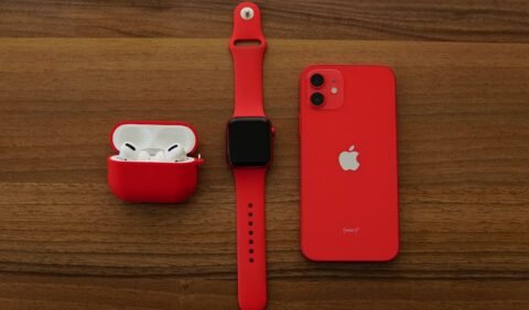iPhone, Apple Watch, dan AirPods berwarna merah di atas meja.