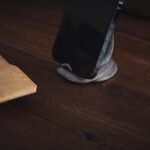Ponsel hitam diletakkan pada holder berbentuk lilitan di atas meja kayu.