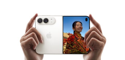 iPhone Duo terbuka dipegang dengan dua tangan, menampilkan kamera belakang dan layar luar dengan foto seseorang.