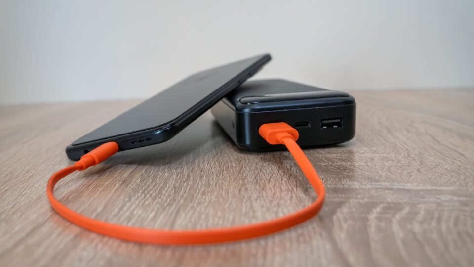 Smartphone terhubung ke powerbank menggunakan kabel oranye di atas meja kayu