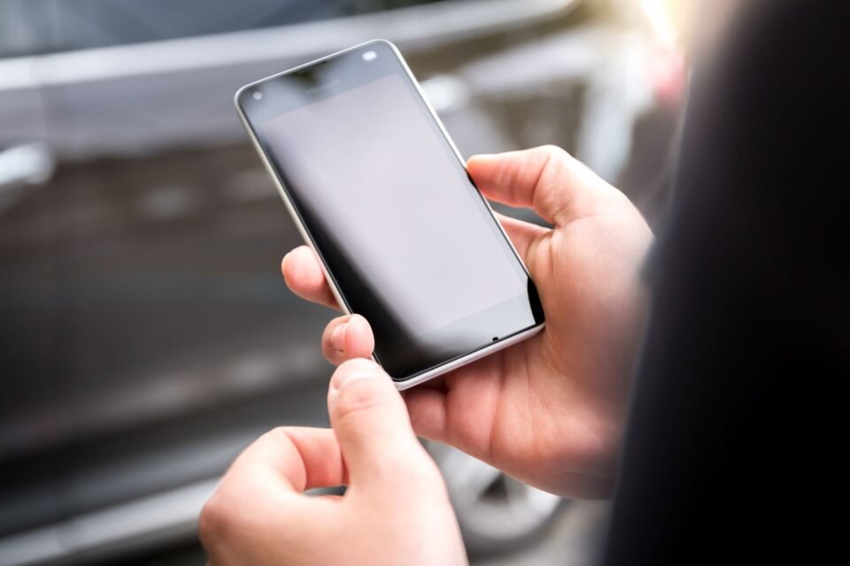 Tangan memegang smartphone dengan layar kosong di dalam ruangan.