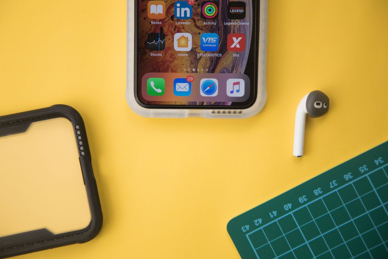 iPhone dengan casing, earbud nirkabel, dan perlengkapan kerja di atas permukaan kuning
