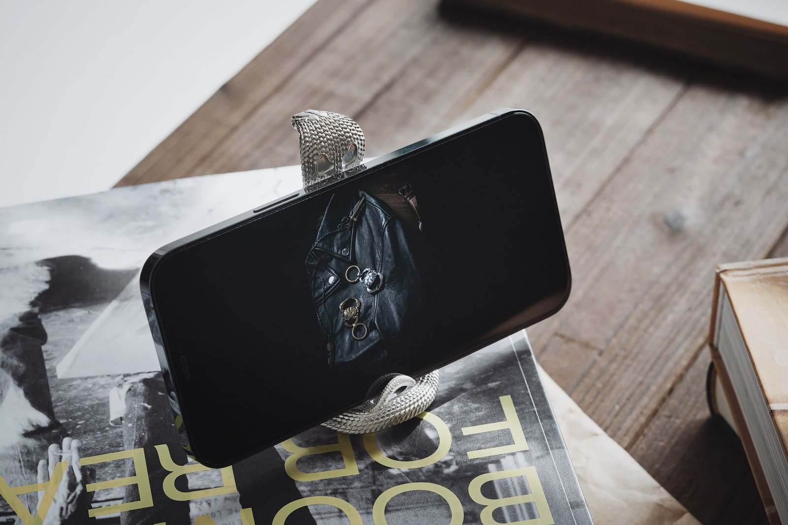 iPhone terpasang pada dudukan berbentuk kobra di atas meja kayu