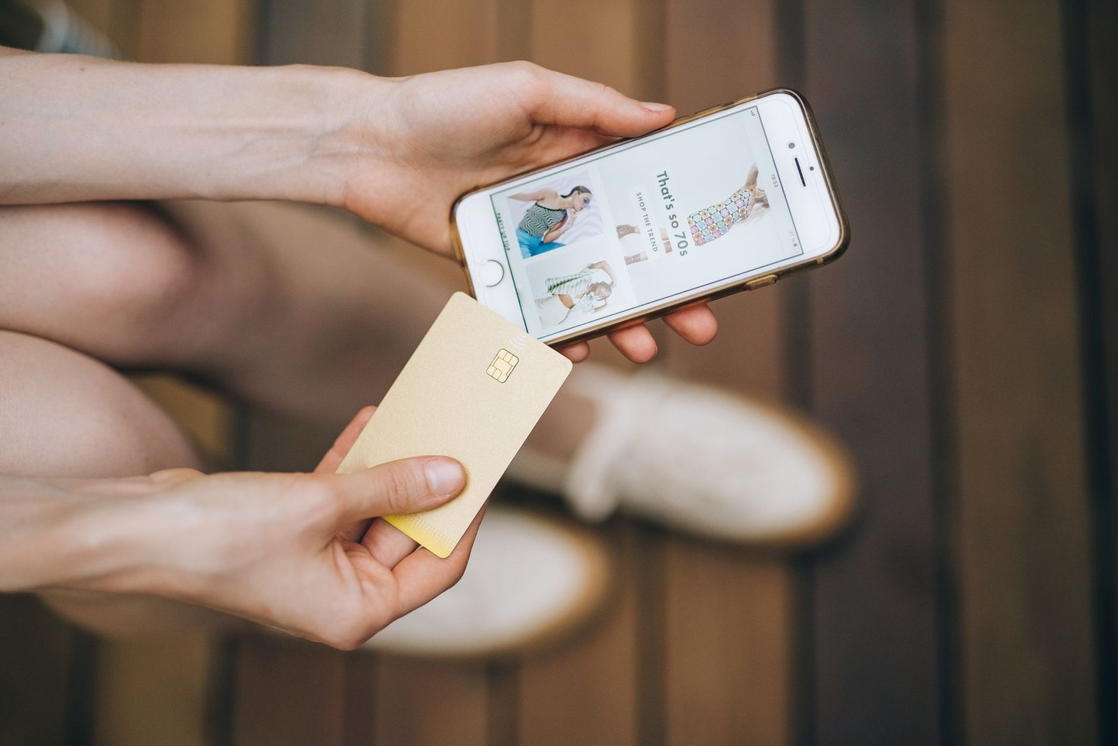 Tangan memegang ponsel yang menampilkan halaman belanja online sambil memegang kartu di dalam ruangan