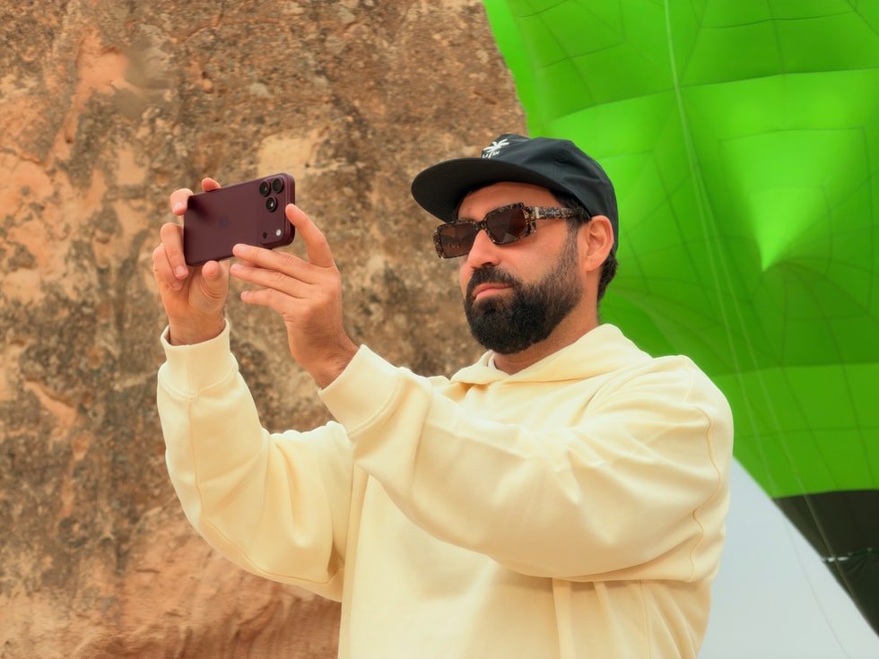 Seorang pria memegang iPhone 18 Pro Max secara horizontal untuk merekam video di luar ruangan.