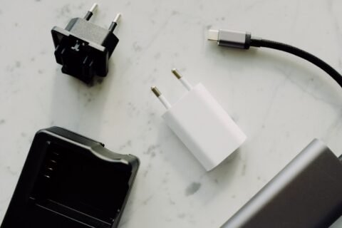 Beberapa adaptor pengisi daya, kabel USB-C, dan aksesori elektronik tersusun di atas permukaan marmer.