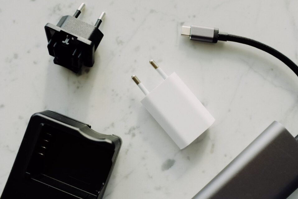 Beberapa adaptor pengisi daya, kabel USB-C, dan aksesori elektronik tersusun di atas permukaan marmer.