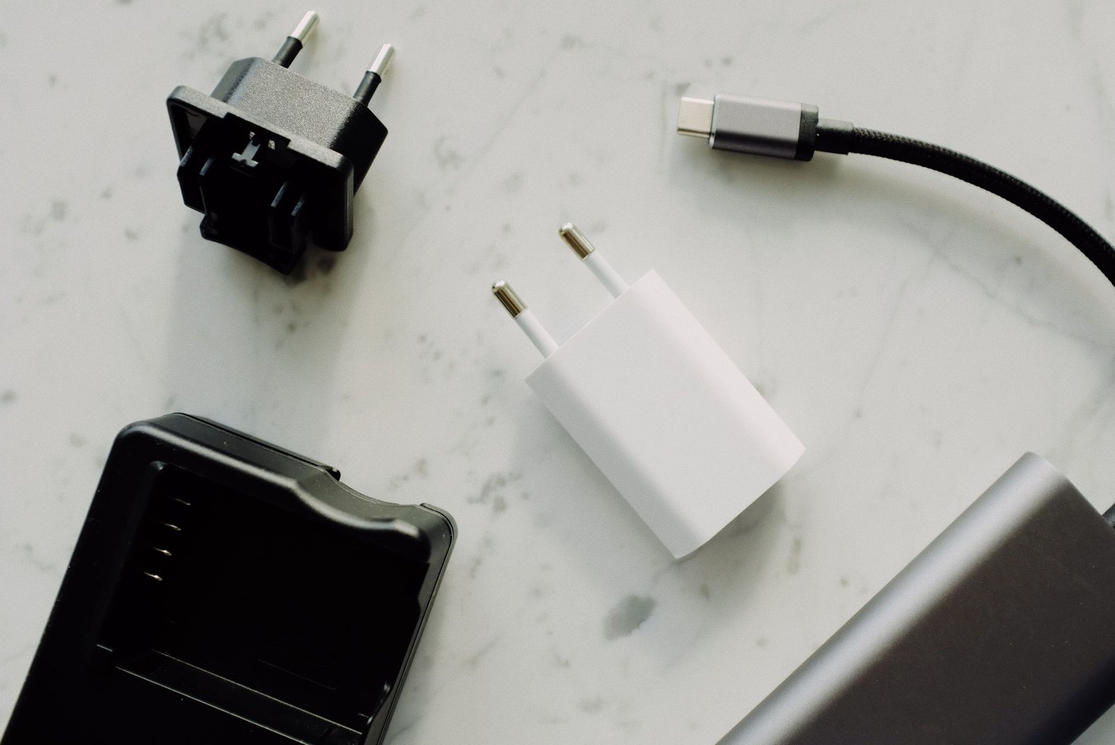 Beberapa adaptor pengisi daya, kabel USB-C, dan aksesori elektronik tersusun di atas permukaan marmer.
