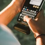 Seseorang mengetik di smartphone yang terhubung ke powerbank saat berada di luar ruangan.