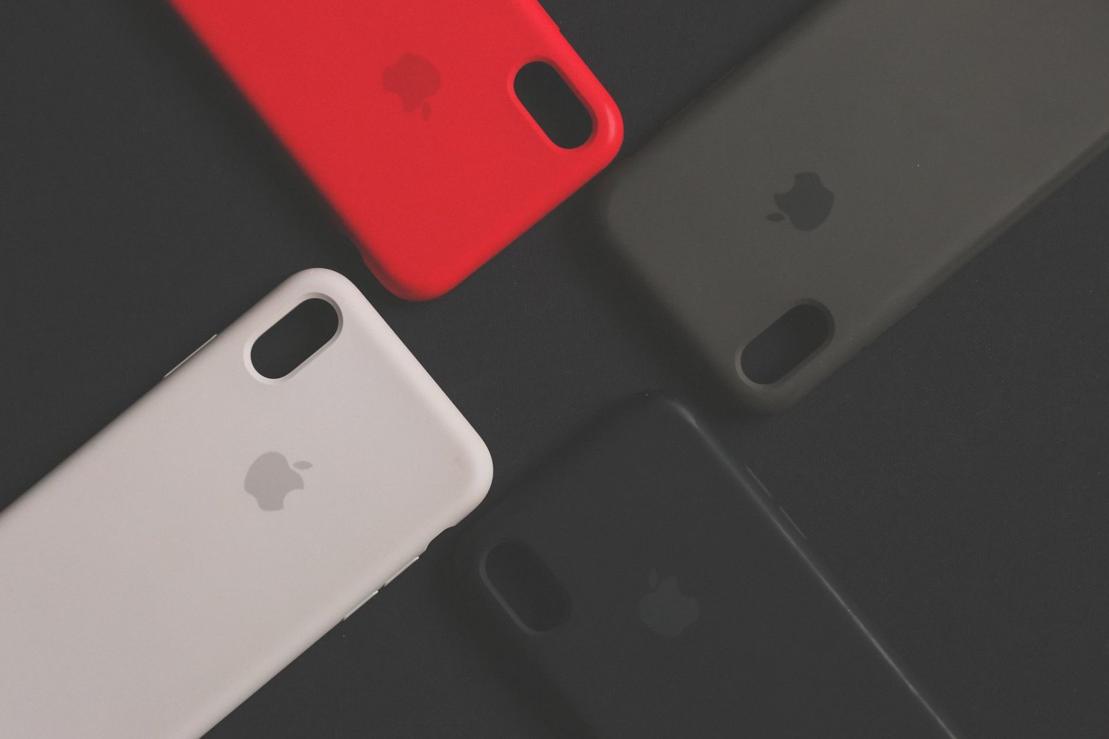 Empat casing iPhone dengan warna dan desain berbeda diletakkan di atas permukaan gelap.