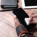 Seseorang membersihkan layar smartphone dengan kain di atas meja kerja