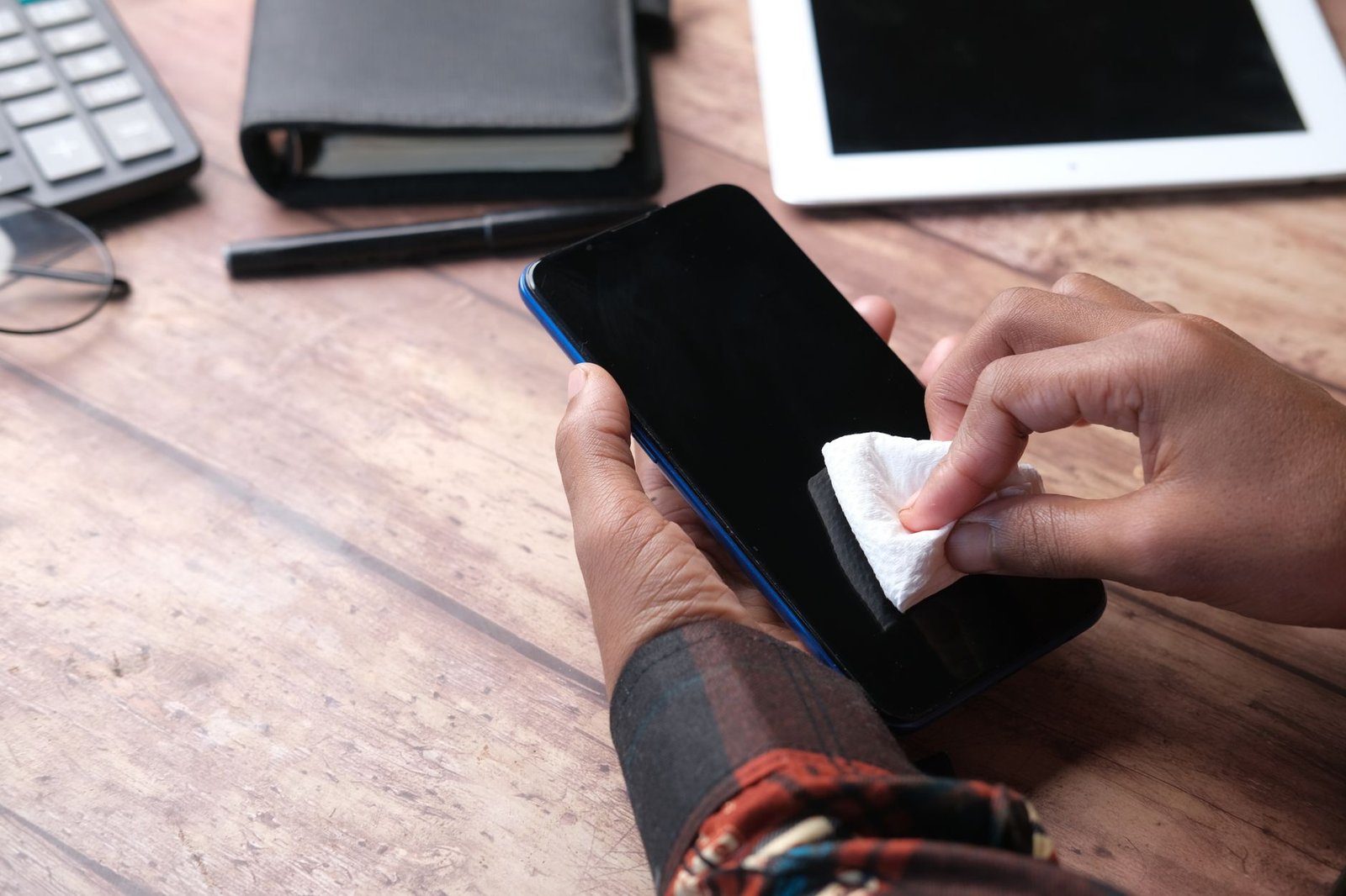 Seseorang membersihkan layar smartphone dengan kain di atas meja kerja