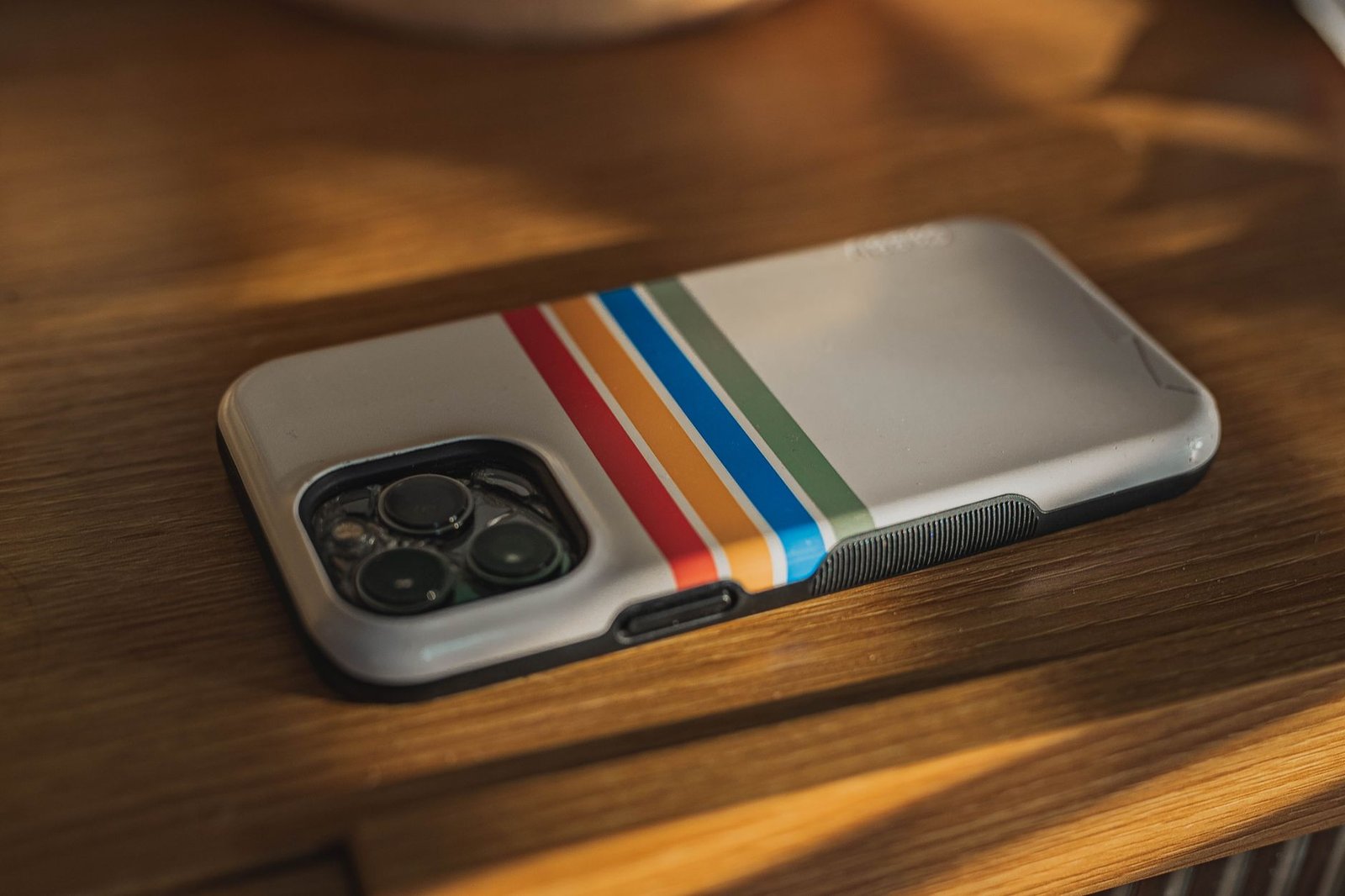 iPhone dengan casing transparan bergaris warna-warni tergeletak di atas permukaan kayu.