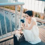 Seorang perempuan duduk di luar ruangan sambil menggunakan kipas portable genggam.