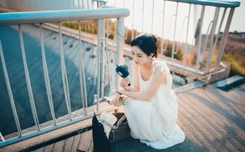 Seorang perempuan duduk di luar ruangan sambil menggunakan kipas portable genggam.