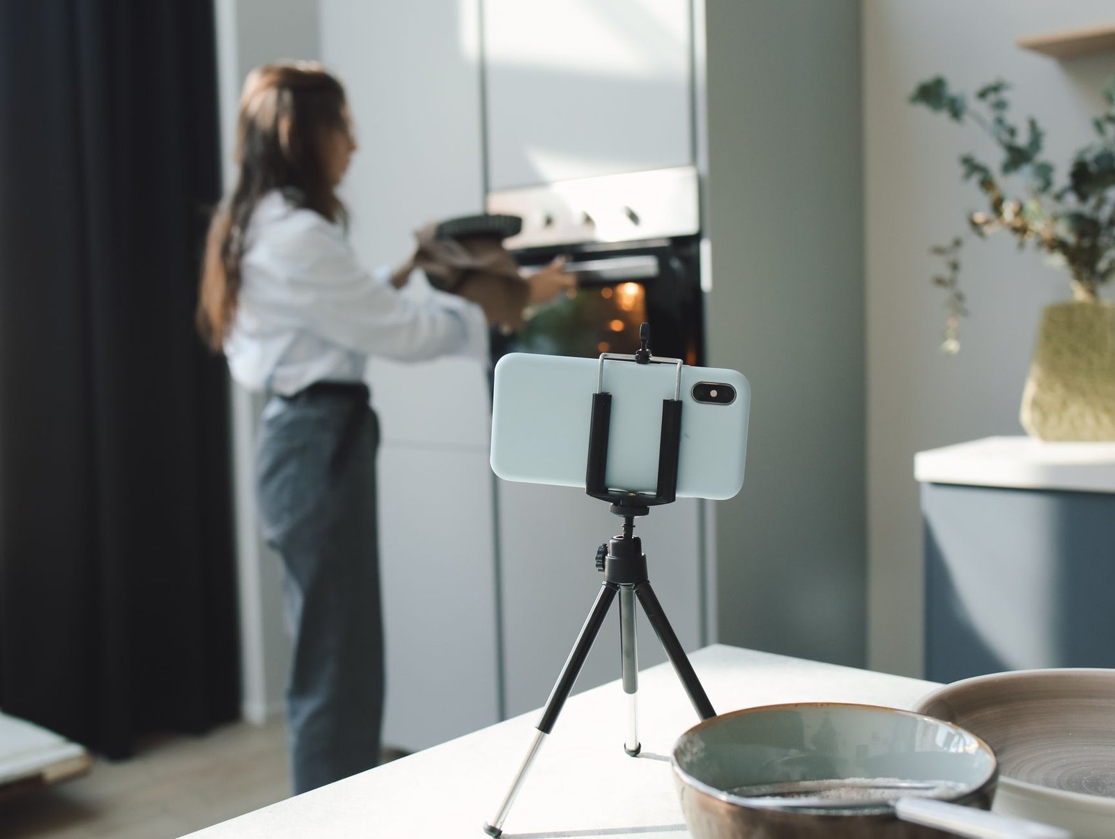 Tripod kecil menopang ponsel untuk merekam proses menata makanan di dapur.