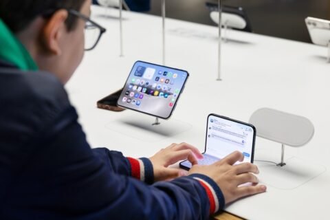 Pengunjung menggunakan iPhone Duo yang terbuka di meja display Apple, dengan perangkat pengisian daya nirkabel terlihat di sampingnya.
