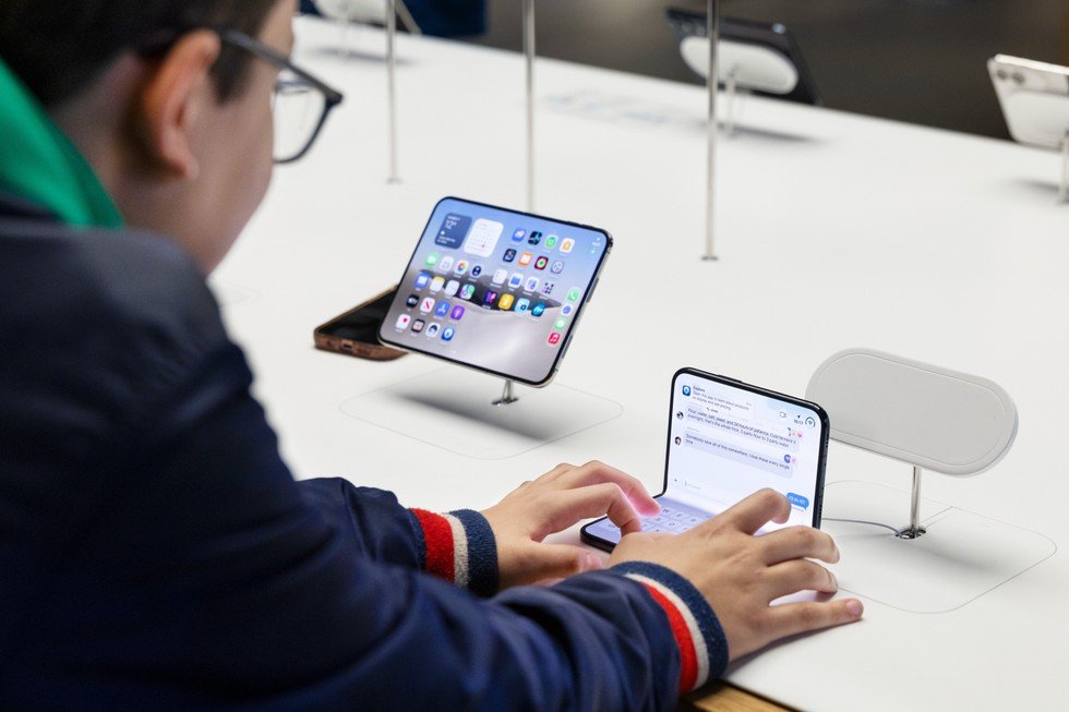 Pengunjung menggunakan iPhone Duo yang terbuka di meja display Apple, dengan perangkat pengisian daya nirkabel terlihat di sampingnya.