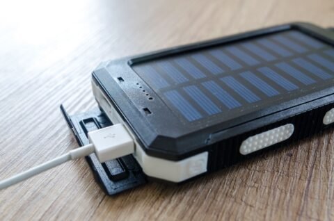 Powerbank tenaga surya hitam dengan kabel USB terhubung, diletakkan di atas meja kayu