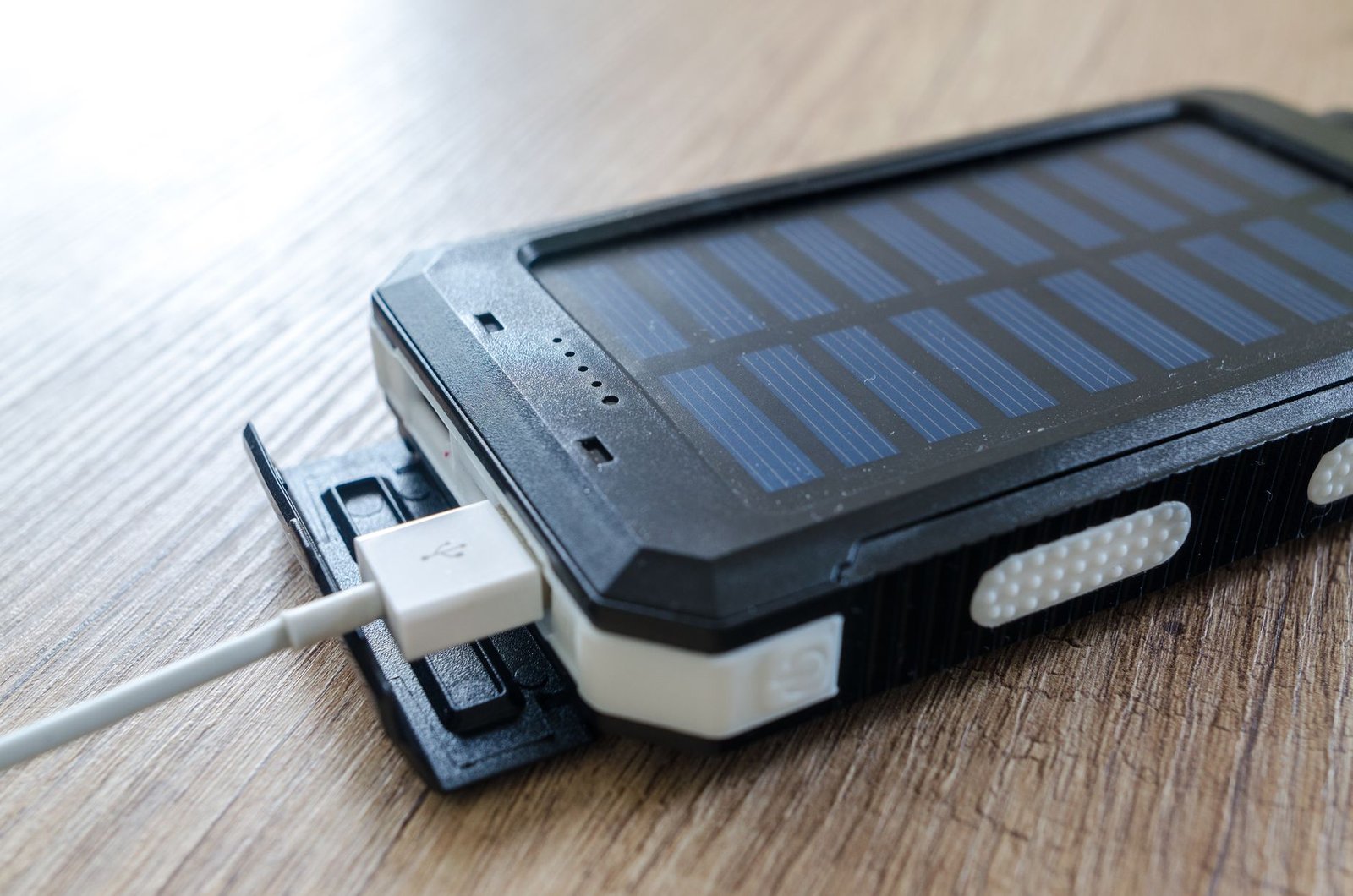 Powerbank tenaga surya hitam dengan kabel USB terhubung, diletakkan di atas meja kayu