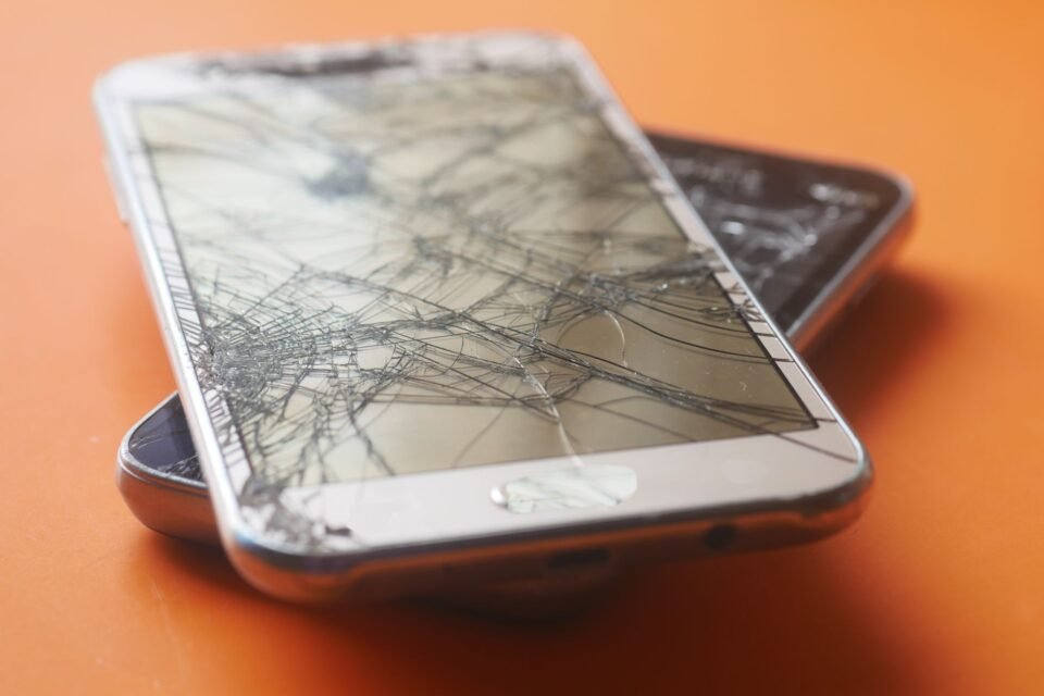 Dua smartphone dengan layar yang retak parah di atas permukaan berwarna oranye