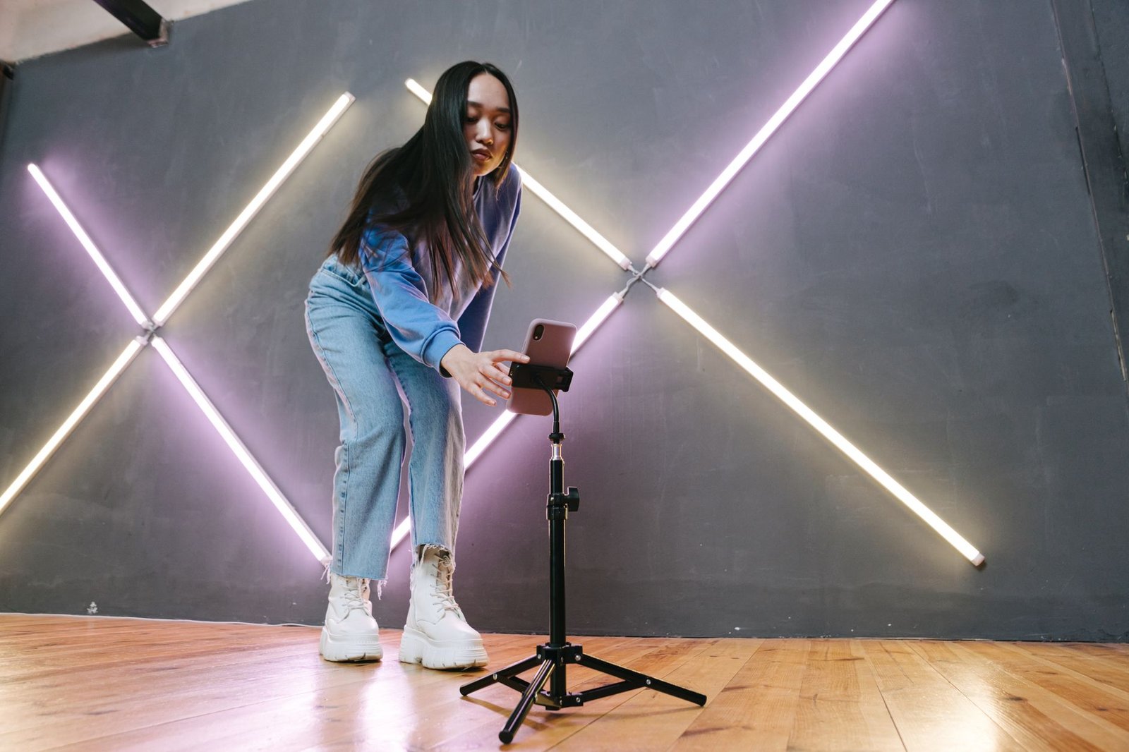 Perempuan mengatur smartphone yang terpasang pada tripod tinggi di ruangan dengan lampu neon.